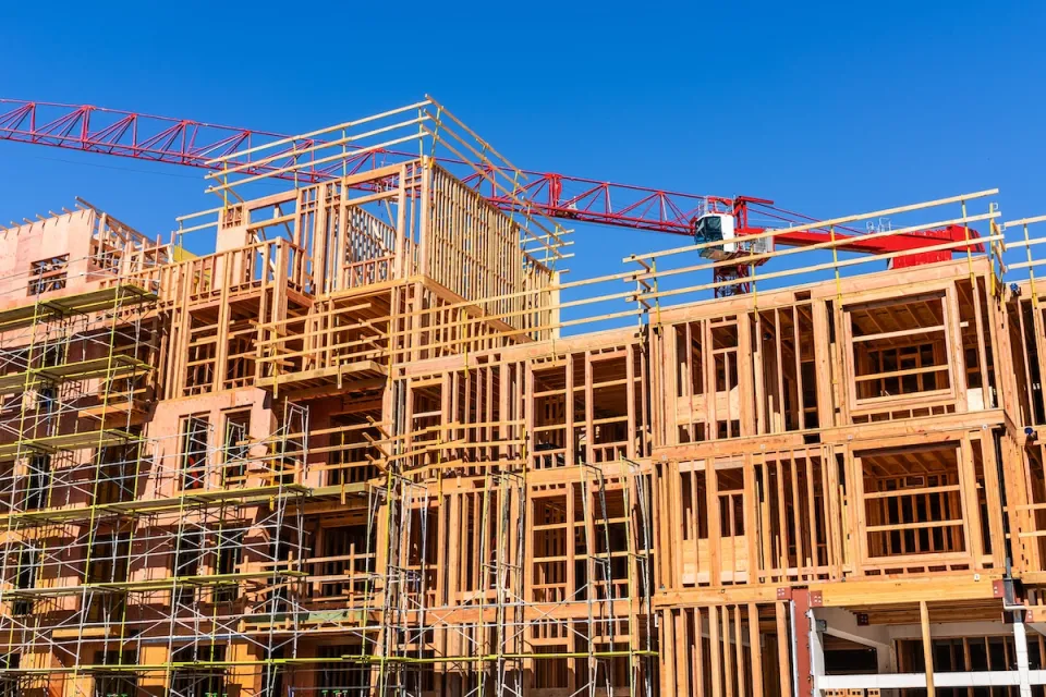 Wood-framed multi-family building under construction with red crane behind it.